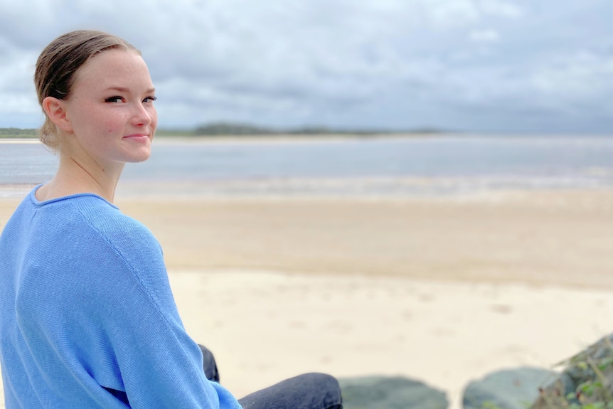 Young woman sitting by the beach, smiling