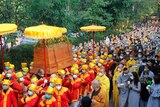 A huge procession of buddhist monks wearing bright red and yellow clothes carry a casket.