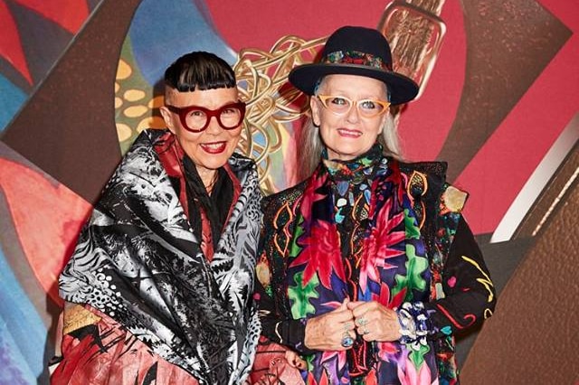 Two people dressed in colourful clothes stand on the red carpet.