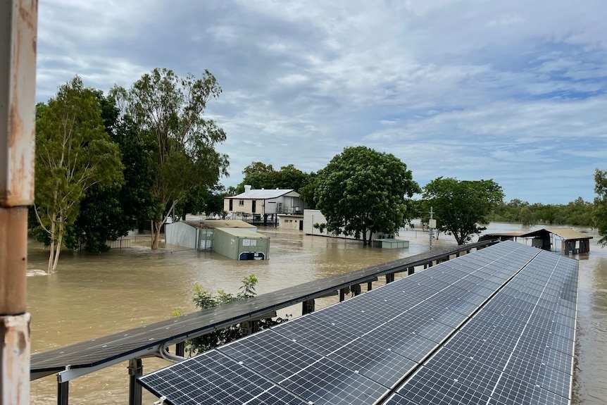 Dark brown water rising up a house on stilts, solar panels and a generator