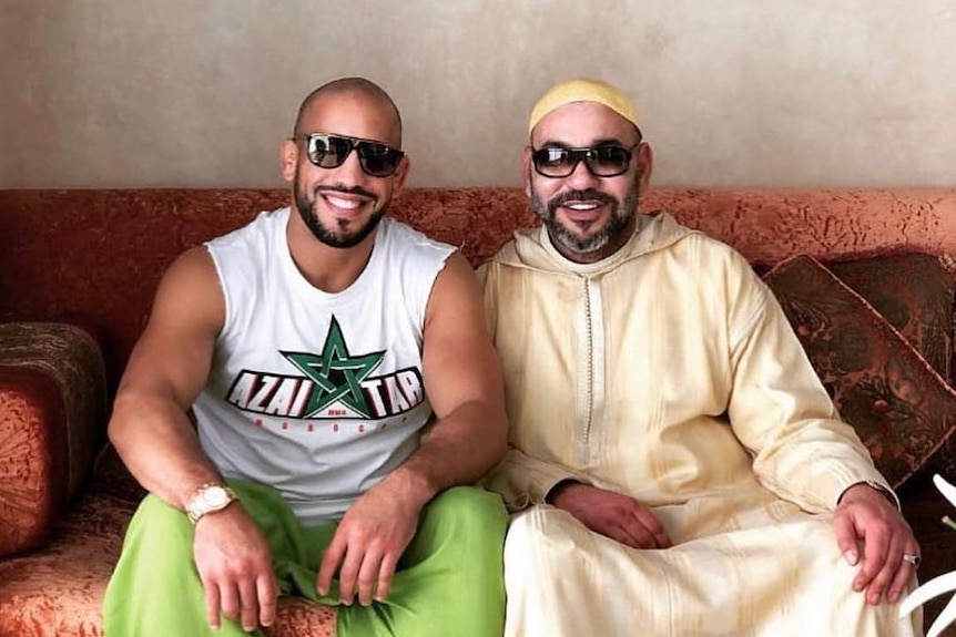 Two men in sunglasses smiling on a couch together 