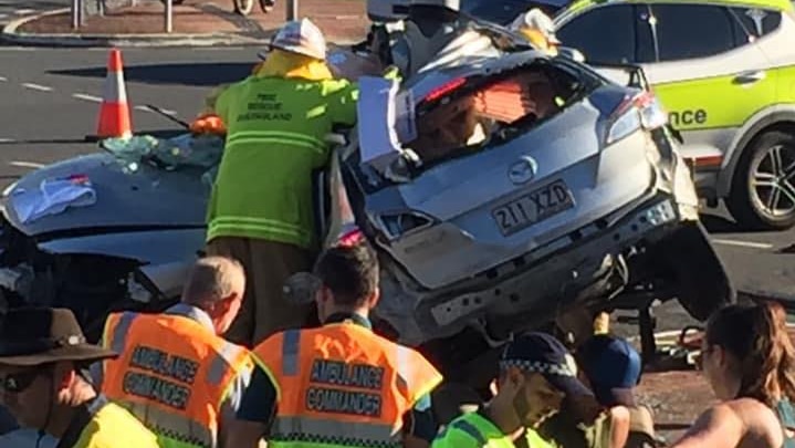 Authorities and bystanders stand near a crashed car which is wrapped around a power pole.