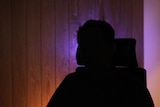 A man sitting on a chair in silhouette to hide his face and identity