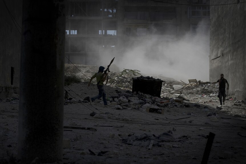 A rebel fighter carrying a rocket-propelled grenade moves across open ground under heavy tank fire in Aleppo.