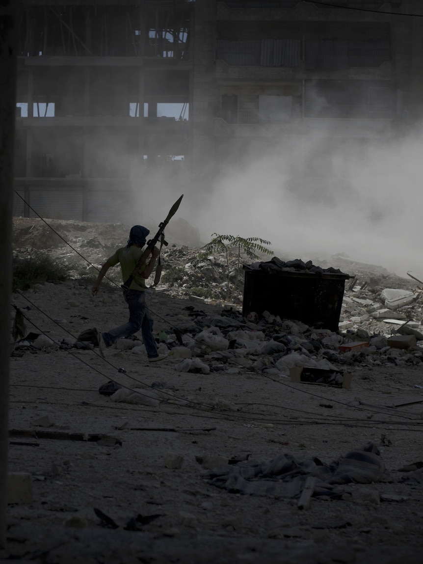 A rebel fighter carrying a rocket-propelled grenade moves across open ground under heavy tank fire in Aleppo.