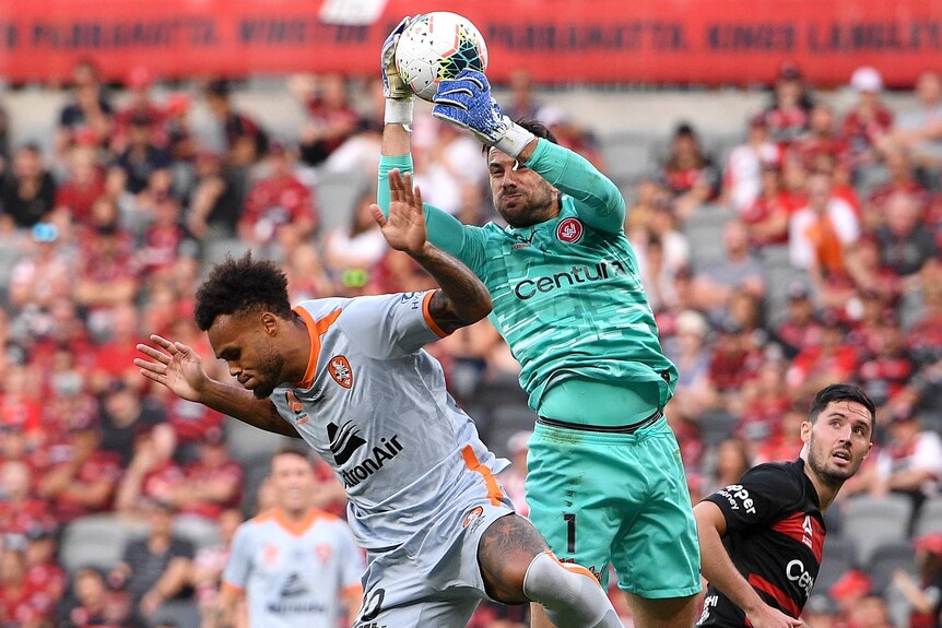 A goalkeeper leaps high to take a ball as an opposition forward puts him under pressure.