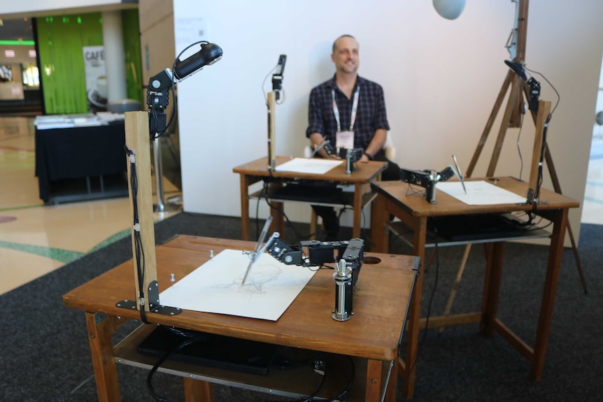 Man sits while robots draw his portrait