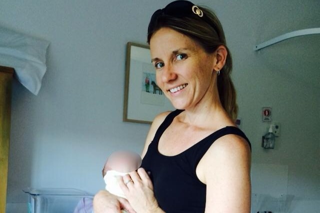 A woman in a black singlet holds a small  baby