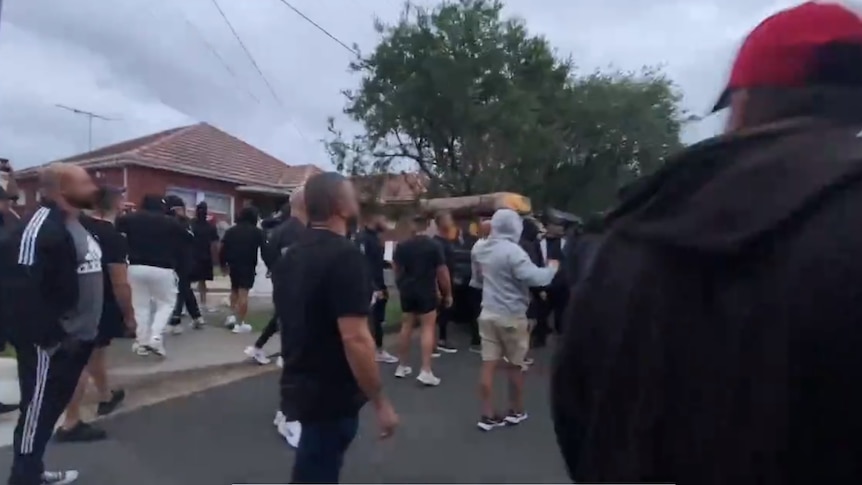 A group of people wearing black tshirts and hoodies standing on a street
