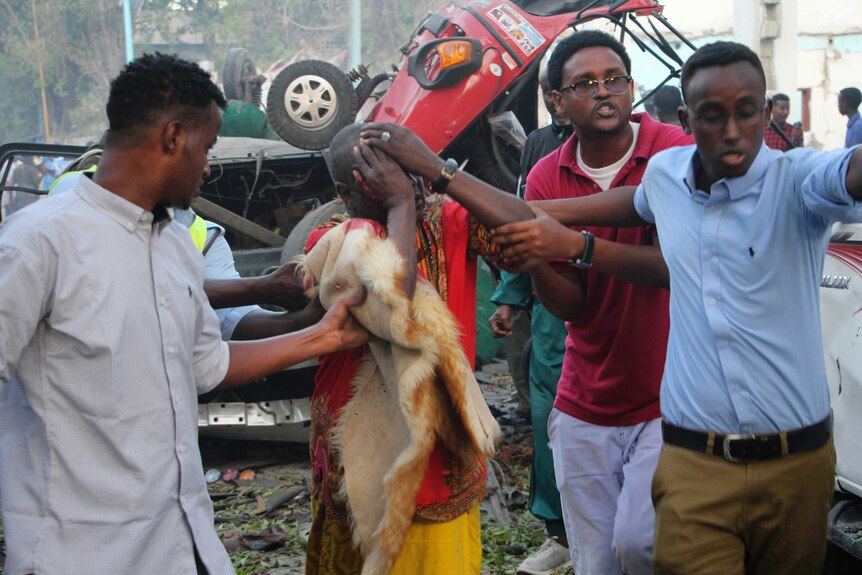 A man covers his face as a crowd helps him away from the wreckage of a car bomb.