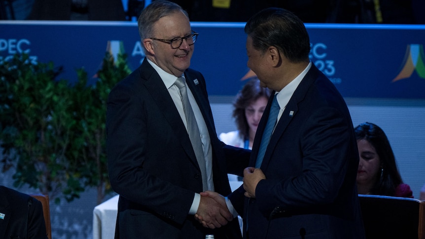 Anthony Albanese smiles while shaking hands with Xi Jinping, whose head is turned away from camera