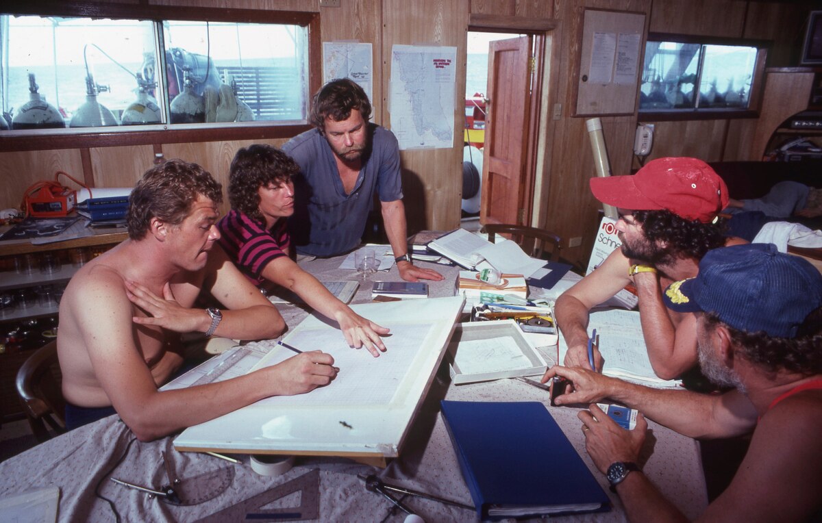 a group of people sit around a table looking at maps
