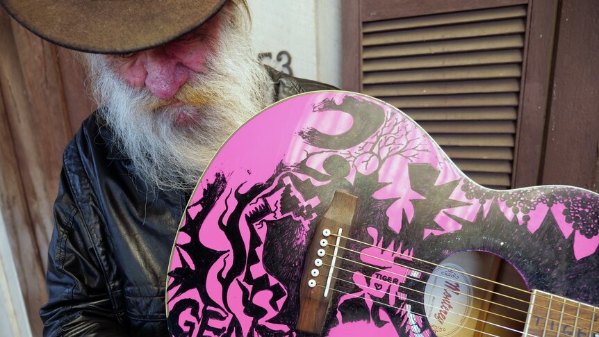 Leon Bozanich looking down away from the camera holding a pink guitar with black writing and designs