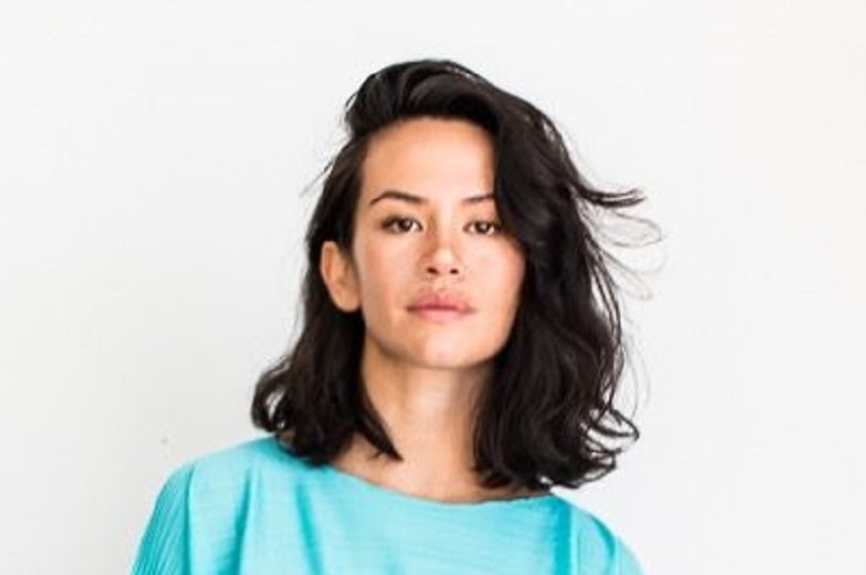 Amrita Hepi, in a light blue dress, stands in front of a white wall.