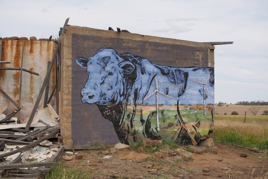 Large mural of a bull, modern windmills in the landscape are painted on the body of the bull. Concrete structure in a paddock.