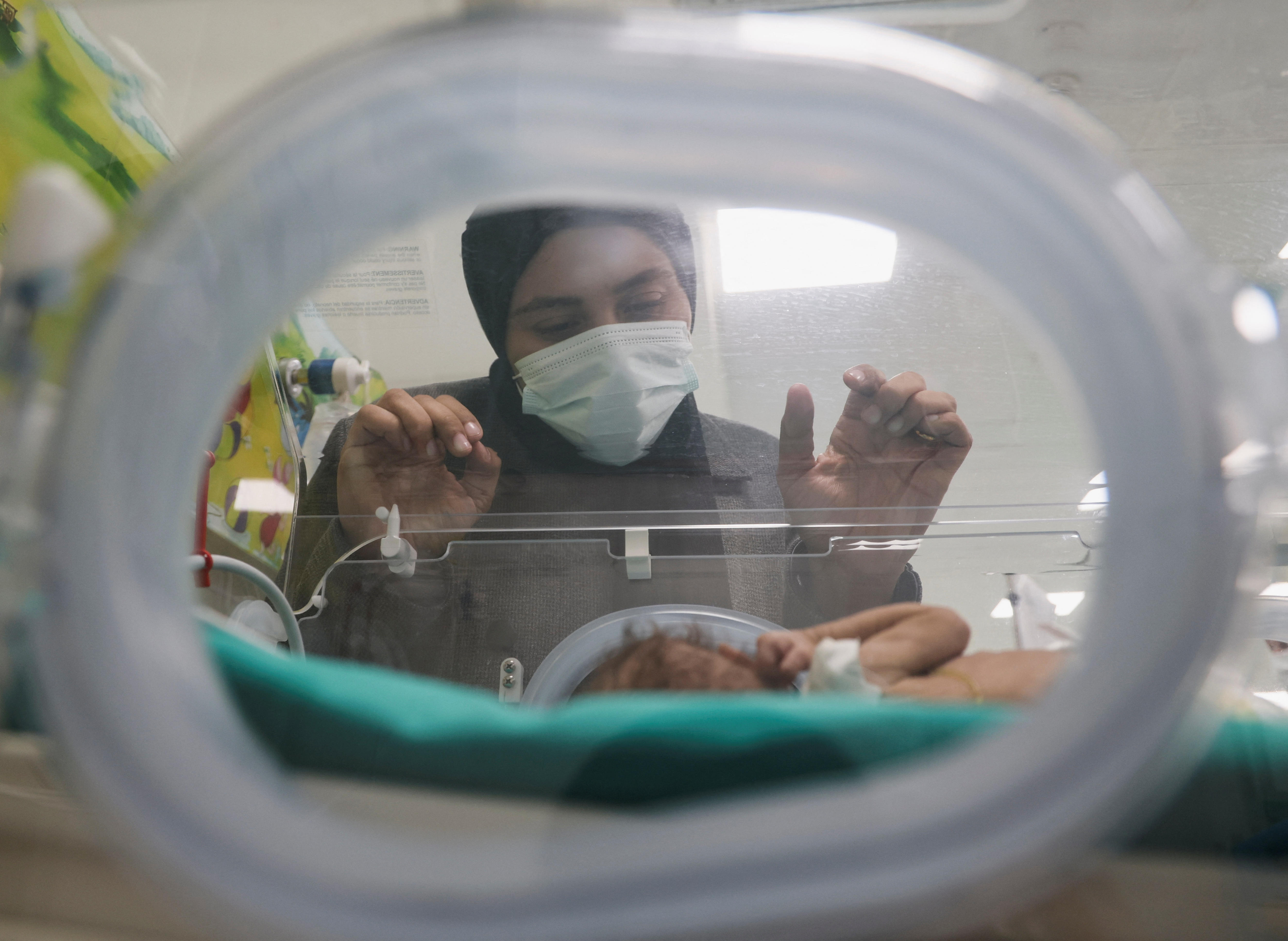 A woman peers into an incubator where her premature baby is seen. 