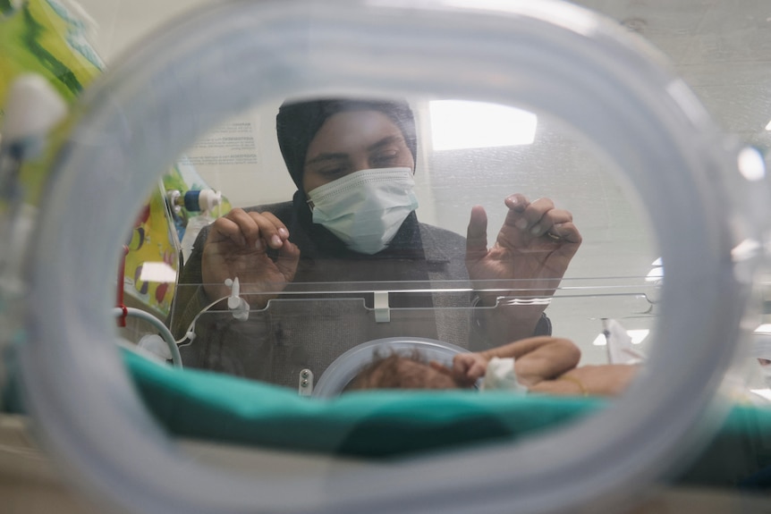 A woman peers into an incubator where her premature baby is seen. 
