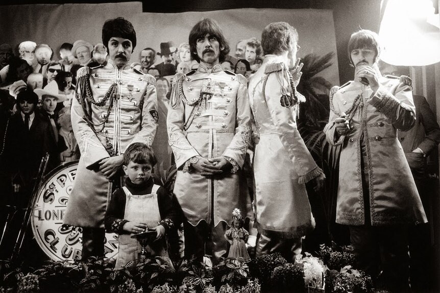 Black and white photo of The Beatles standing in front of cardboard while shooting the cover of Sgt Pepper's album.