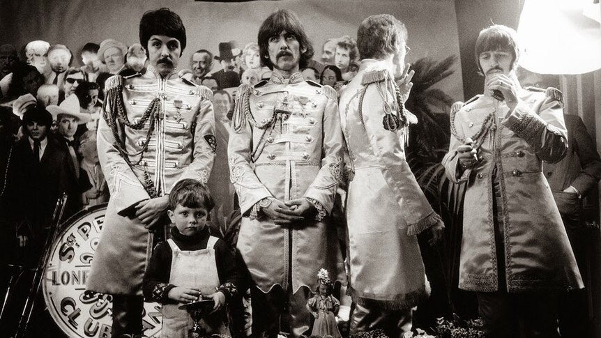 Black and white photo of The Beatles standing in front of cardboard while shooting the cover of Sgt Pepper's album.
