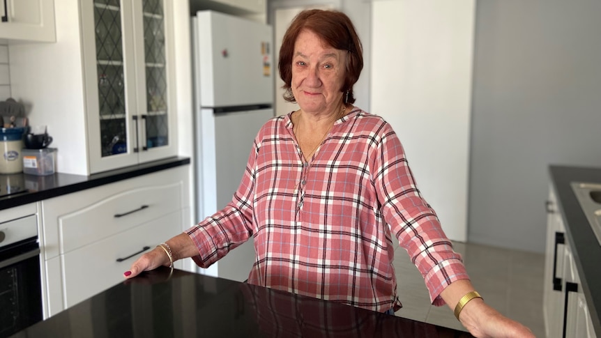 A woman in a pink shirt stands at her new marble benchtop surround by glossy white walls and new appliances.