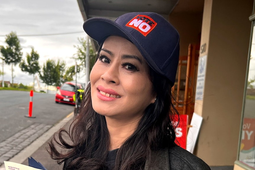 Sunny Lu smiles, wearing a 'VOTE NO' cap as she stands on a suburban street.