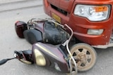 A scooter is seen trapped under the front wheels of a red truck.