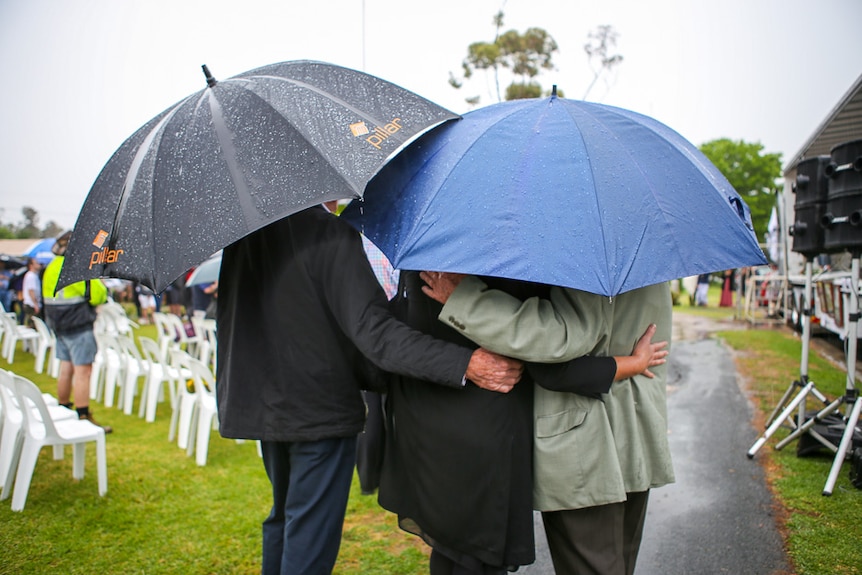 Three memorial attendees embrace under their umbrellas.