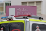 A sign says jeta gardens with an ambulance in the foreground.