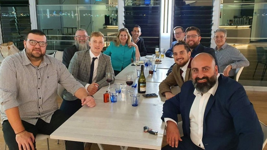 Hollie Hughes and nine other people sitting around a table, turning to smile at a camera. On the table are glasses of wine.