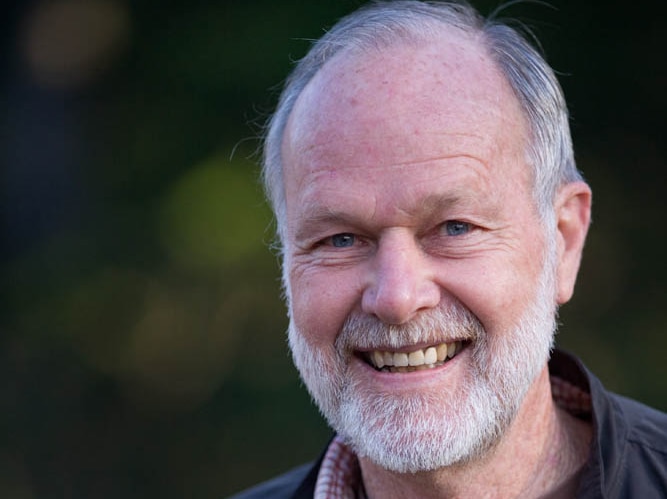 A bearded man smiles for a portrait outside on a sunny day.