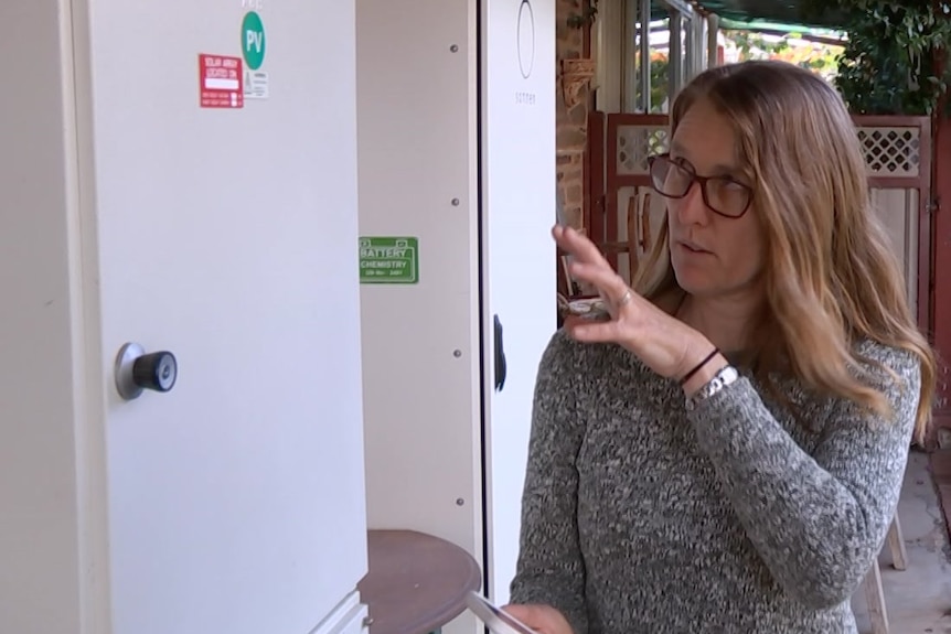 A woman gesticulating at a cabinet on her outside wall