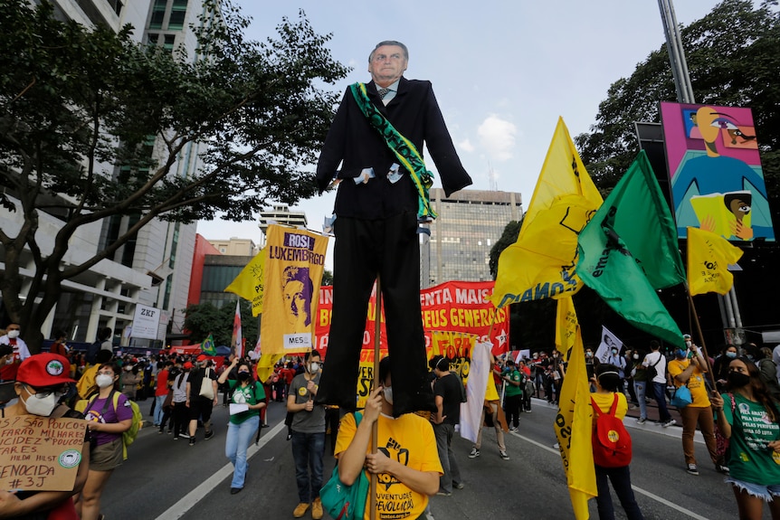 Una donna che cammina a una manifestazione di protesta tiene in mano un grande ritratto ritagliato di Jair Bolsonaro 