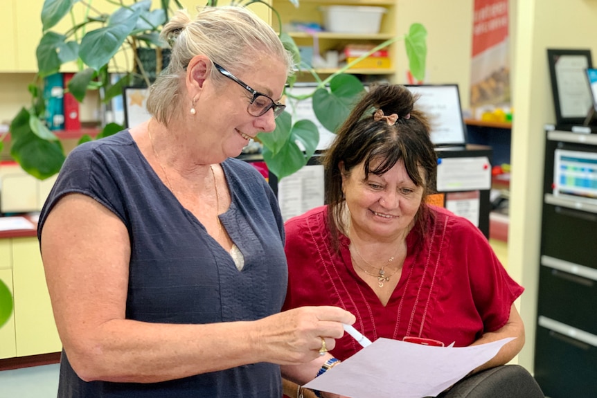 Two women in an office smiling as they look at paperwork