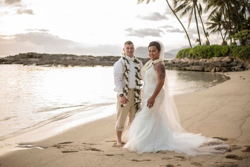A woman in a wedding dress stands next to a man on a tropical beach