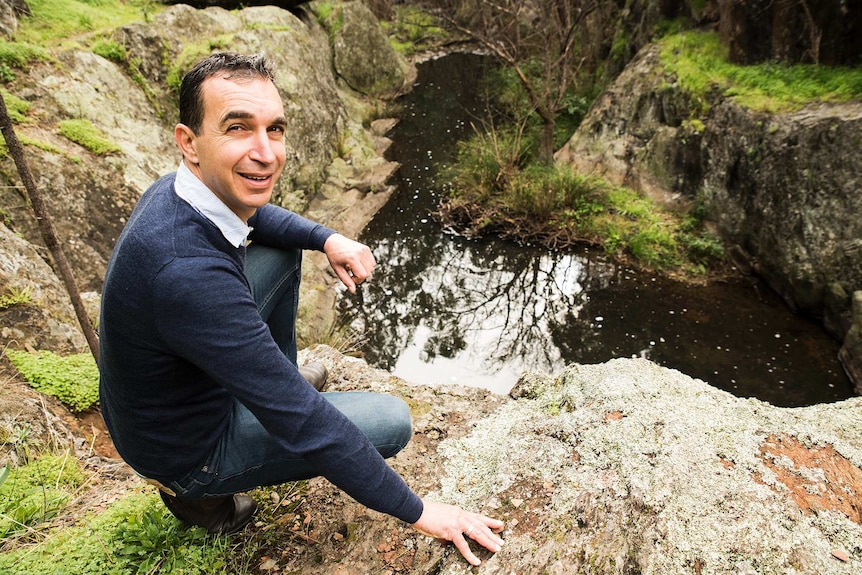 Jason van Weenen sits on a cliff overlooking water at Sturt Gorge.