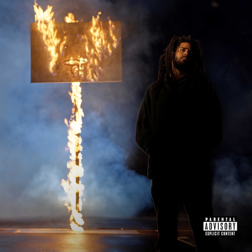 Photograph of J. Cole with basketball ring in background on fire.