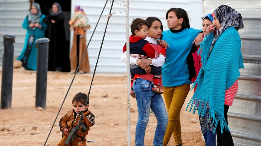 Children gather in a circle, while older women stand in the background.