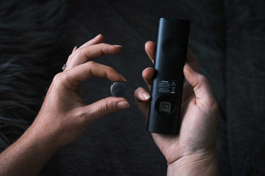 A remote control and its battery as demonstrated with woman's hands only