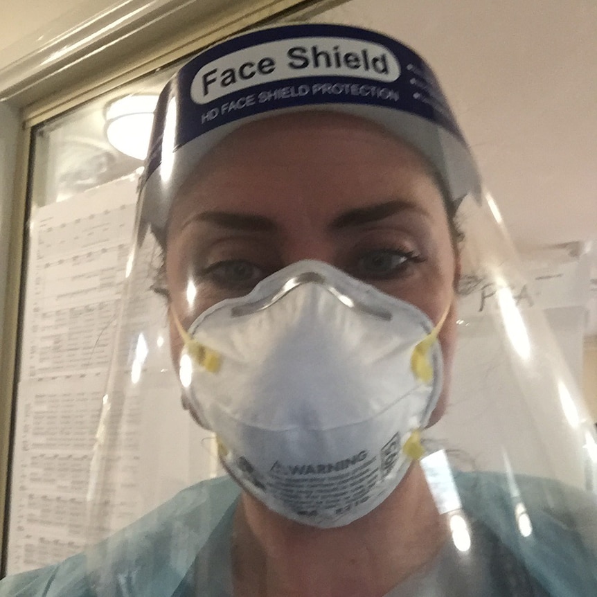 A woman wears full PPE gear including a face shield.