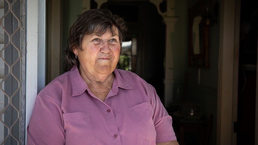 Woman in pink shirt standing in doorway and looking into distance