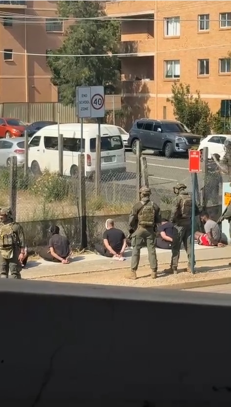 Men sitting on the ground with their hands behind their back.