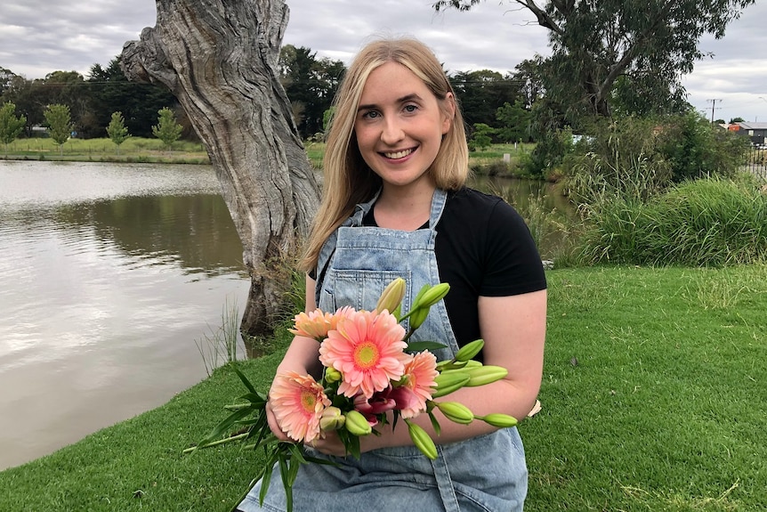 A florist holding up a bunch of flowers near a lake.
