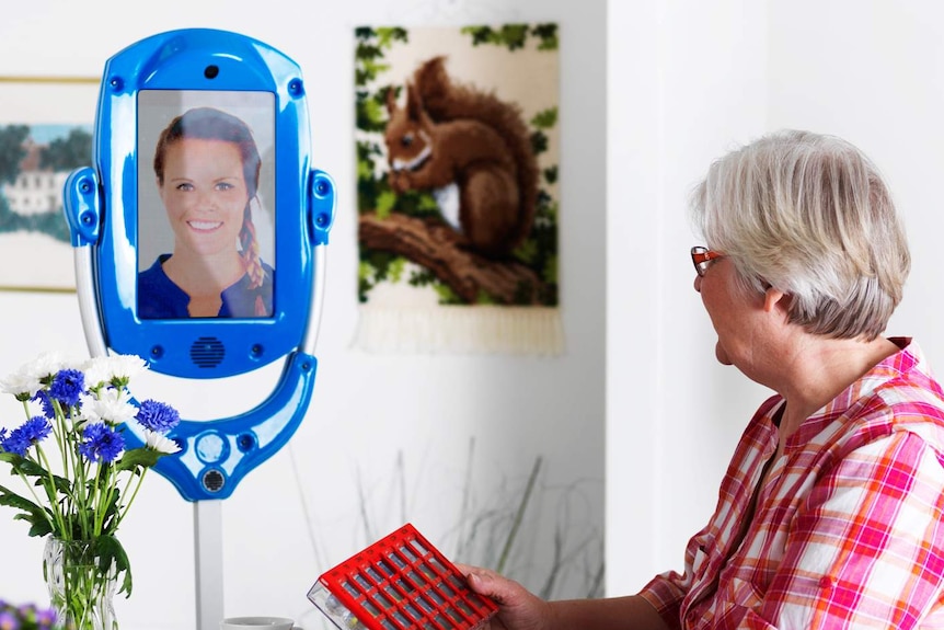 An older person looking at a telepresence robot with a picture of a younger person on the screen