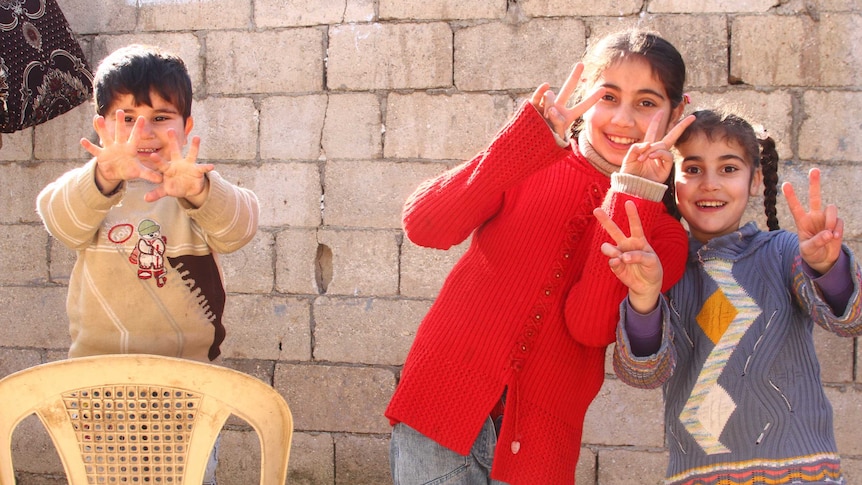 Two girls and a small boy hold up their fingers to the camera.