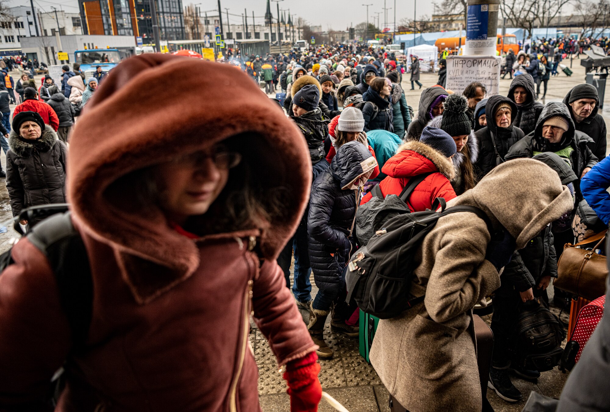 A long line of people, stand five abreast in thick winter coats.  