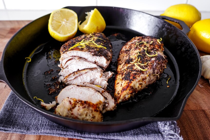 Cooked chicken breast and a halved lemon in a black skillet on a stovetop