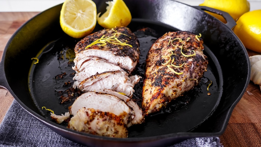 Cooked chicken breast and a halved lemon in a black skillet on a stovetop