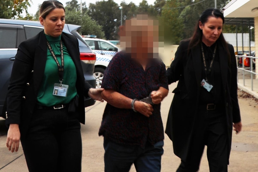 A handcuffed woman whose face is heavily blurred is led towards a building by two female police officers. 