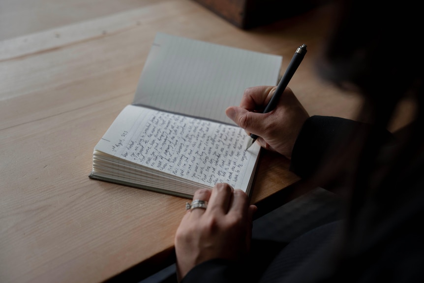 A woman's hand writes in a journal