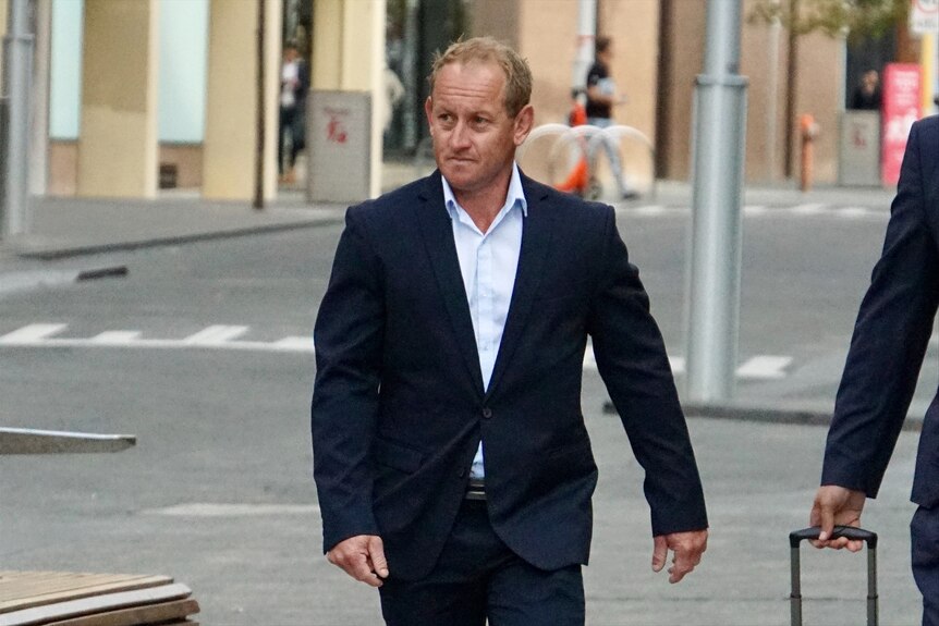 A middle-aged man with fair hair wearing a dark-coloured suit and light shirt walks outside court in Perth.